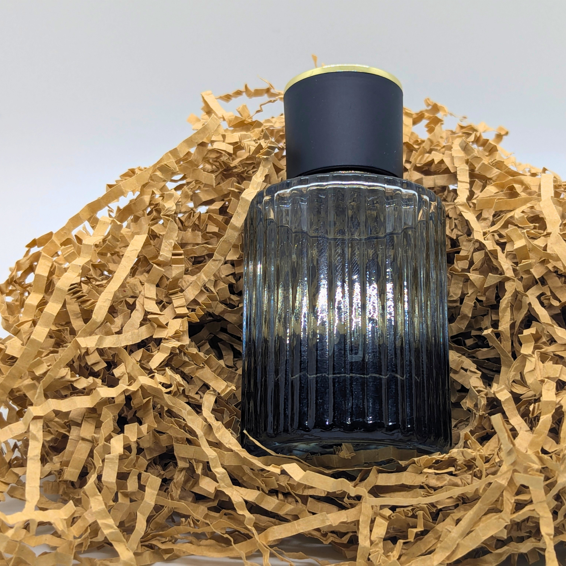 Dark glass bottle with ribbed design on a bed of straw against a light background
