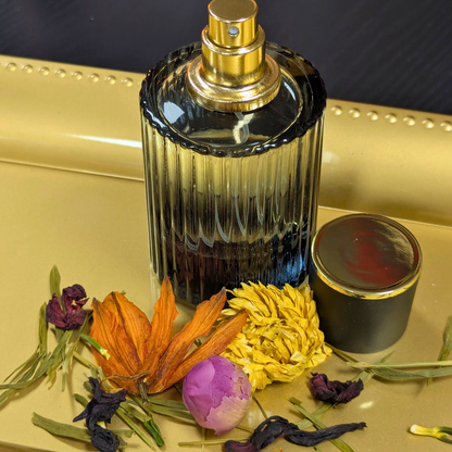 Perfume bottle with gold cap on a reflective surface with flowers and a small container.