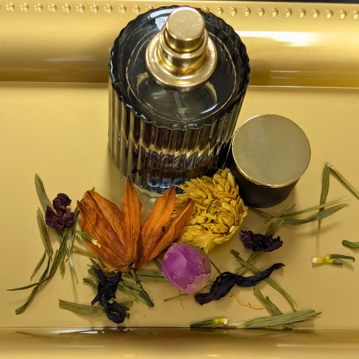 Perfume bottle with dried flowers and herbs on a reflective surface