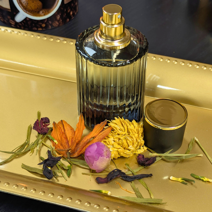 Perfume bottle with gold cap on a decorative tray with flowers and a cup of coffee in the background