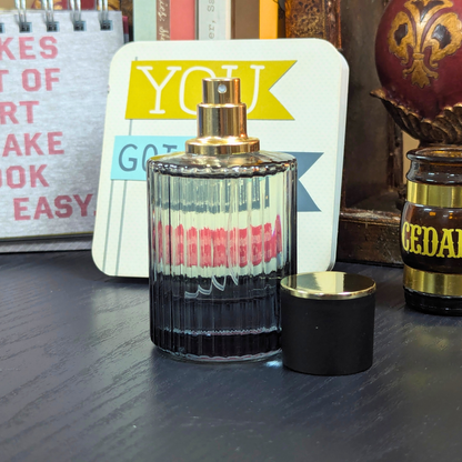 Perfume bottle with gold cap and black base on a wooden surface, with a colorful card and another product in the background.