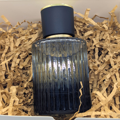 Decorative glass bottle with ribbed design and dark blue cap on crinkled paper background